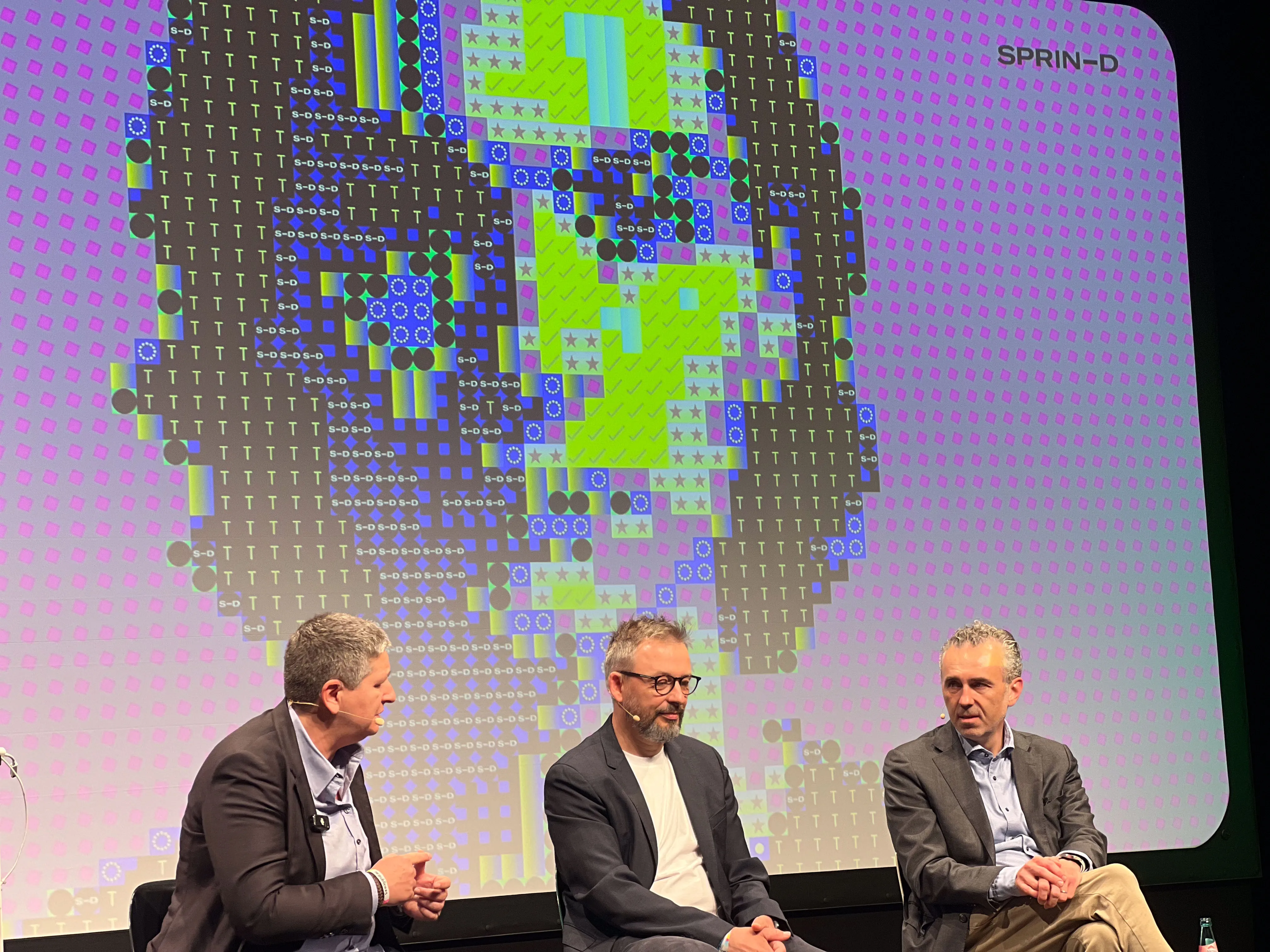 Paneldiskussion auf der re:publica 2025 vor der laufenden Identity-Mirror-Installation — drei Sprecher, im Hintergrund das generative Portrait auf der SPRIND-Leinwand