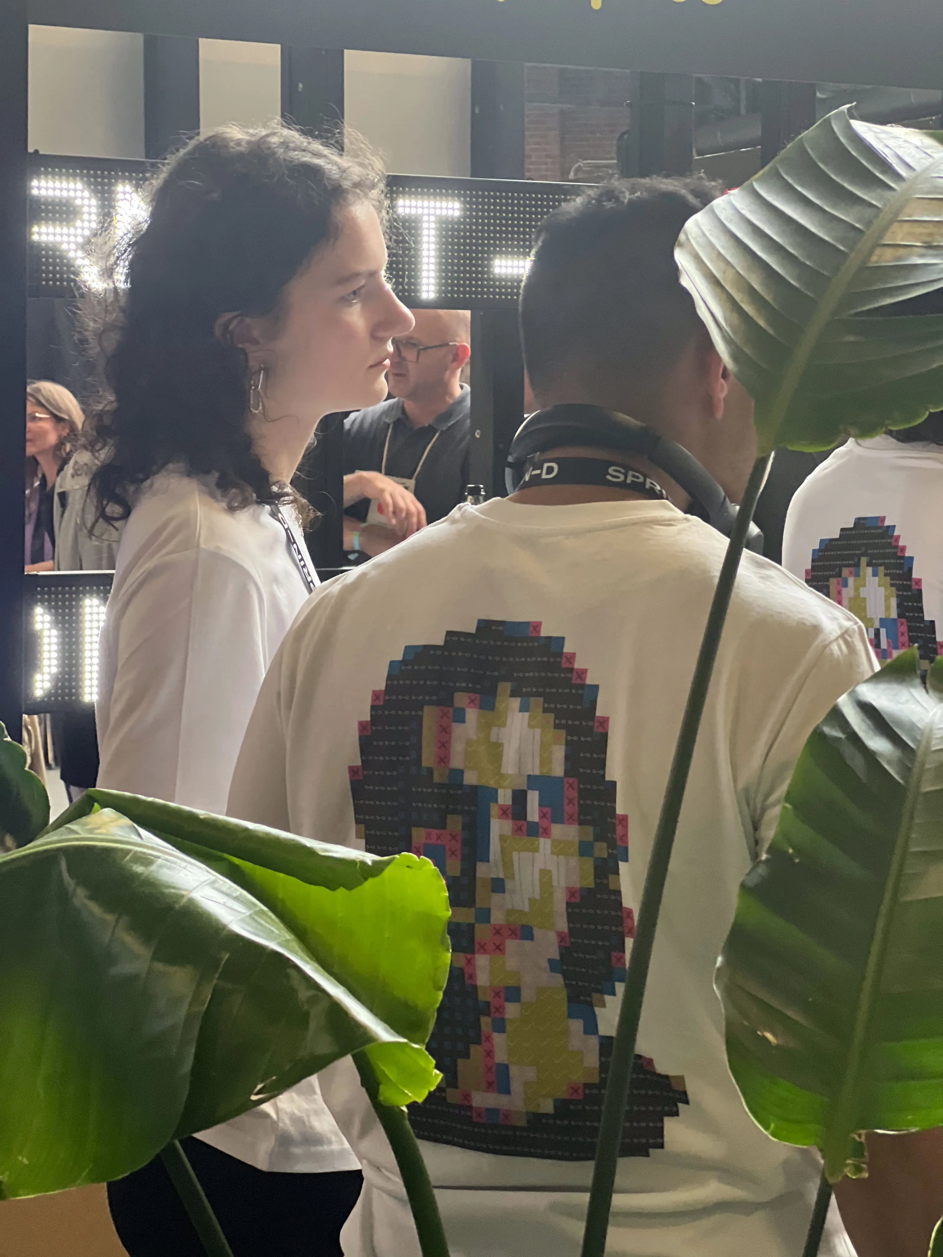 Besucherin auf der re:publica vor der Identity-Mirror-Installation — im Hintergrund das pixelierte Portrait auf dem Bildschirm, Pflanzen im Vordergrund